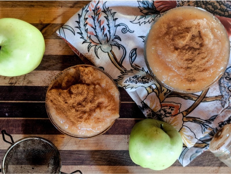 overhead image of two applesauce bowls and two green apples