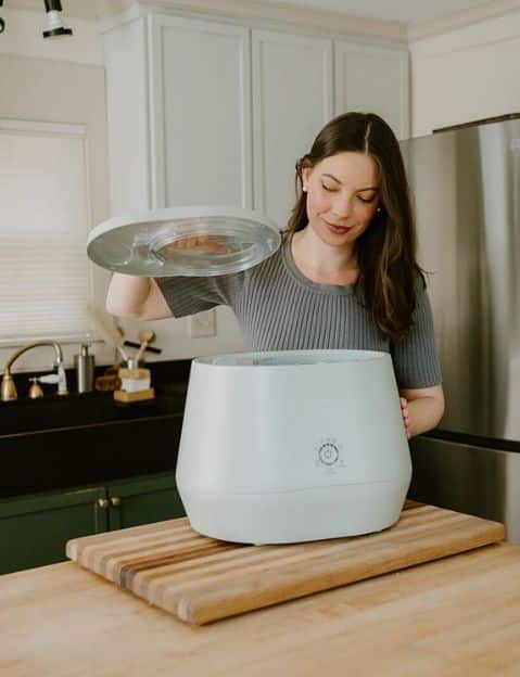 Woman using her kitchen composter in a Lomi composter review post.